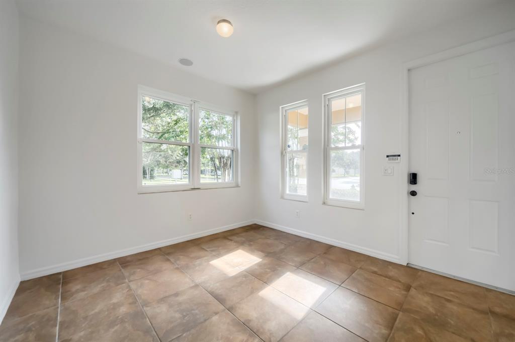 An empty room with white walls, tile flooring, three windows, and a white entry door — 14778 PEEKSKILL DRIVE, WINTER GARDEN, FL