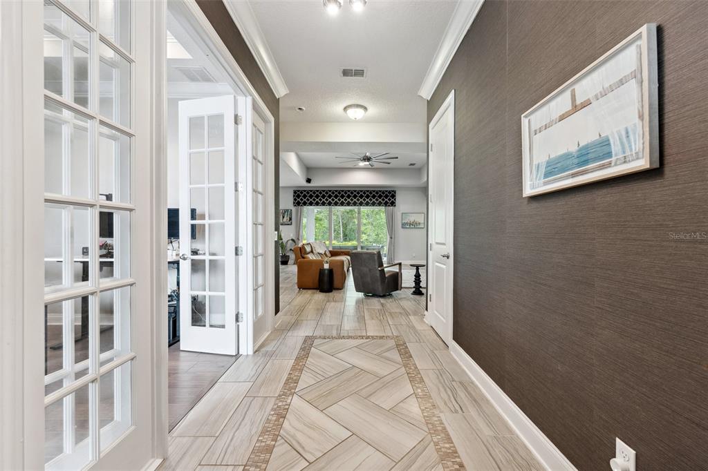 A hallway with tiled flooring and dark textured wallpaper leads toward a living room area — 13137 LOWER HARDEN AVENUE, ORLANDO, FL