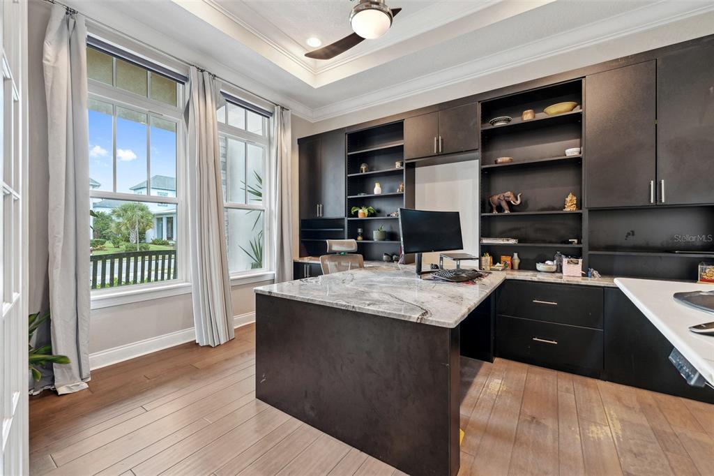A home office features a large stone-topped desk, dark built-in cabinetry, and tall windows — 13137 LOWER HARDEN AVENUE, ORLANDO, FL