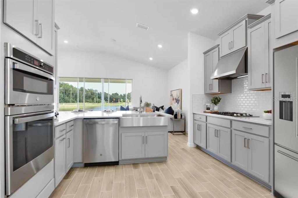 A modern kitchen features gray cabinets, stainless steel appliances, a farmhouse sink, and wood-look flooring — 5772 MEADS BAY POND ROAD, KISSIMMEE, FL
