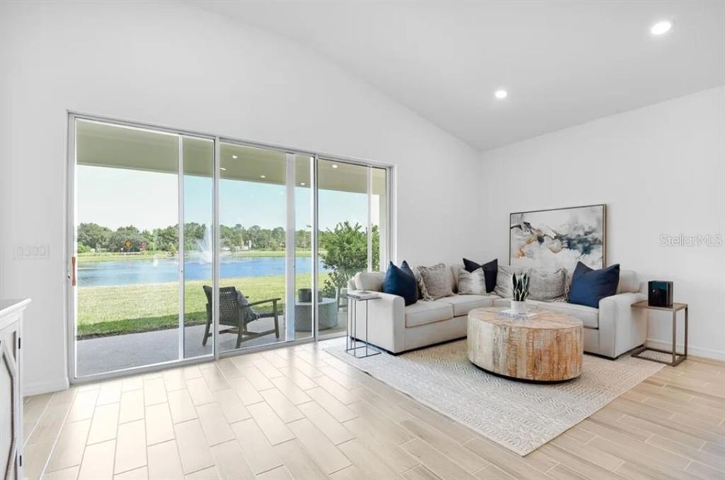 A living room with light tile floors, a sectional sofa, and sliding doors overlooking a lake — 5772 MEADS BAY POND ROAD, KISSIMMEE, FL