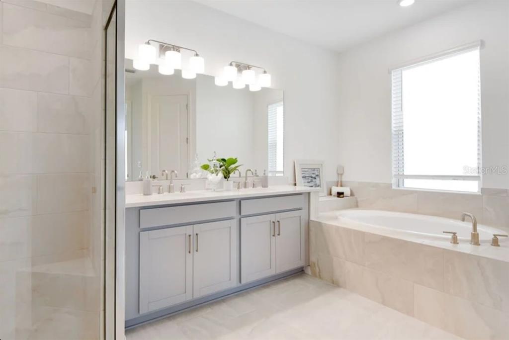 A bathroom features a gray double vanity, a large mirror, and a tiled soaking tub — 5772 MEADS BAY POND ROAD, KISSIMMEE, FL