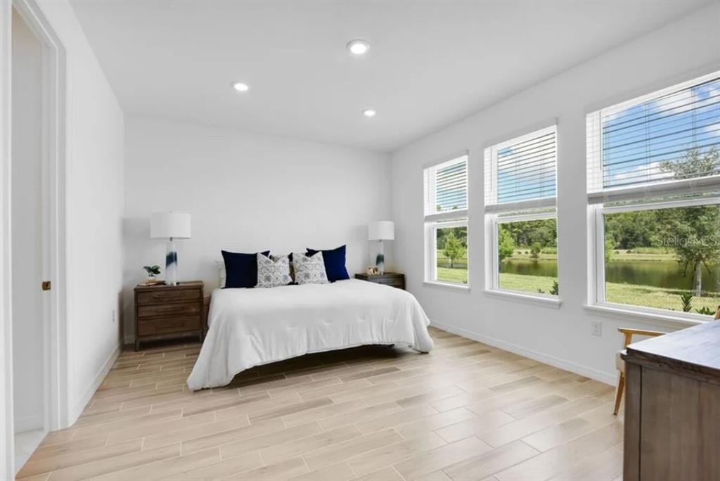 A bedroom with light wood-look tile flooring, a bed, and windows overlooking a pond — 5772 MEADS BAY POND ROAD, KISSIMMEE, FL