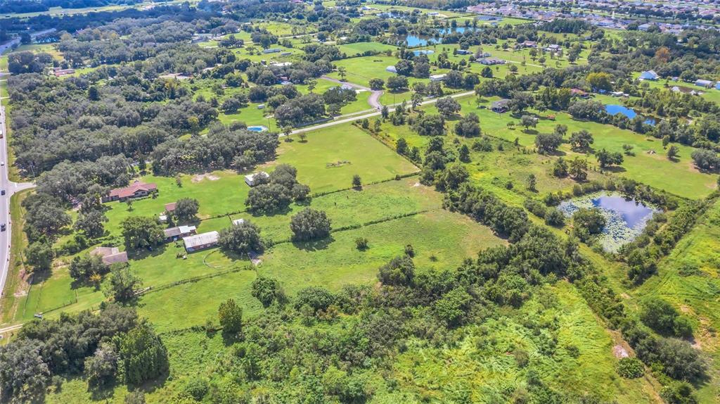 An aerial view of a rural property featuring houses, open green fields, and a pond — 4281 TIMBER LANE, KISSIMMEE, FL