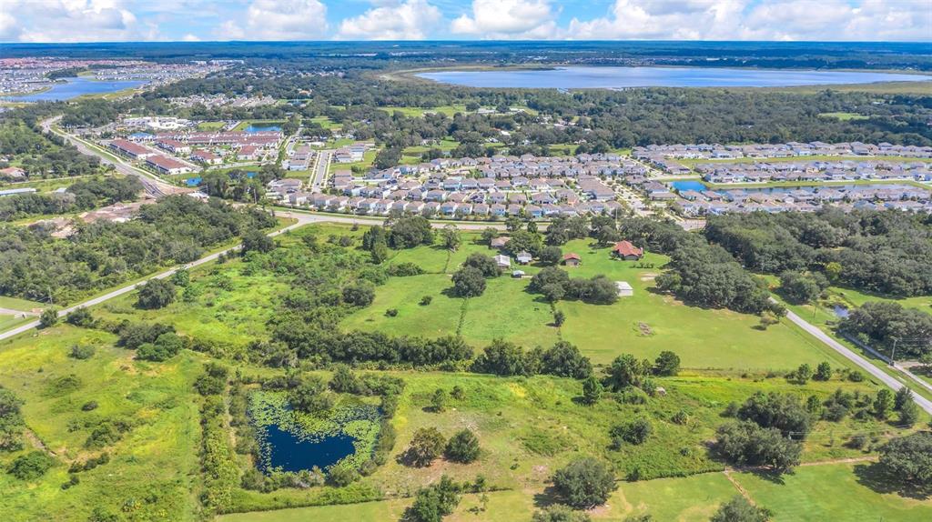 An aerial view shows a large grassy lot with a pond, trees, and surrounding residential developments — 4281 TIMBER LANE, KISSIMMEE, FL