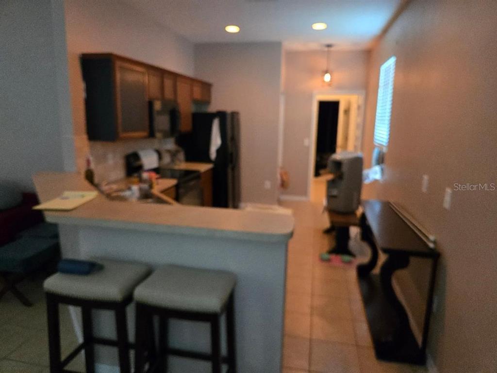 A kitchen with a breakfast bar, dark wood cabinets, and tile flooring leads to a hallway — 2633 WALDEN WOODS DRIVE, PLANT CITY, FL