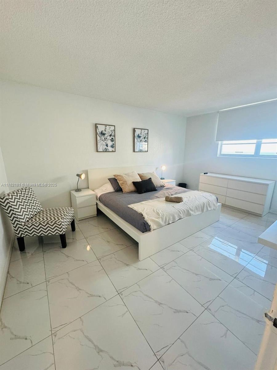 A bedroom features a white bed, marble-style tile flooring, and a patterned accent chair — 3901 S Ocean Dr # 10G, Hollywood FL 33019, HOLLYWOOD, FL
