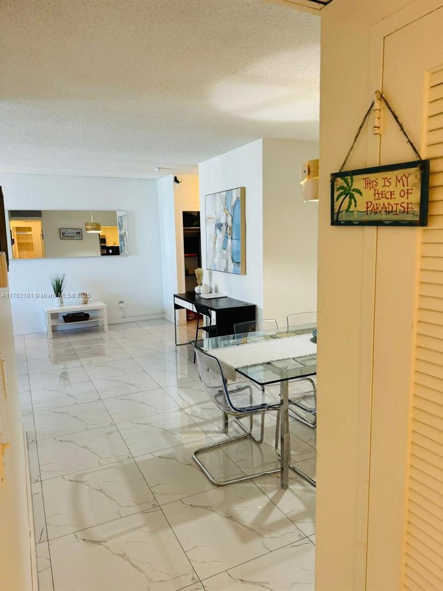 A bright dining and living area features white tile floors, a glass table, and wall art — 3901 S Ocean Dr # 10G, Hollywood FL 33019, HOLLYWOOD, FL