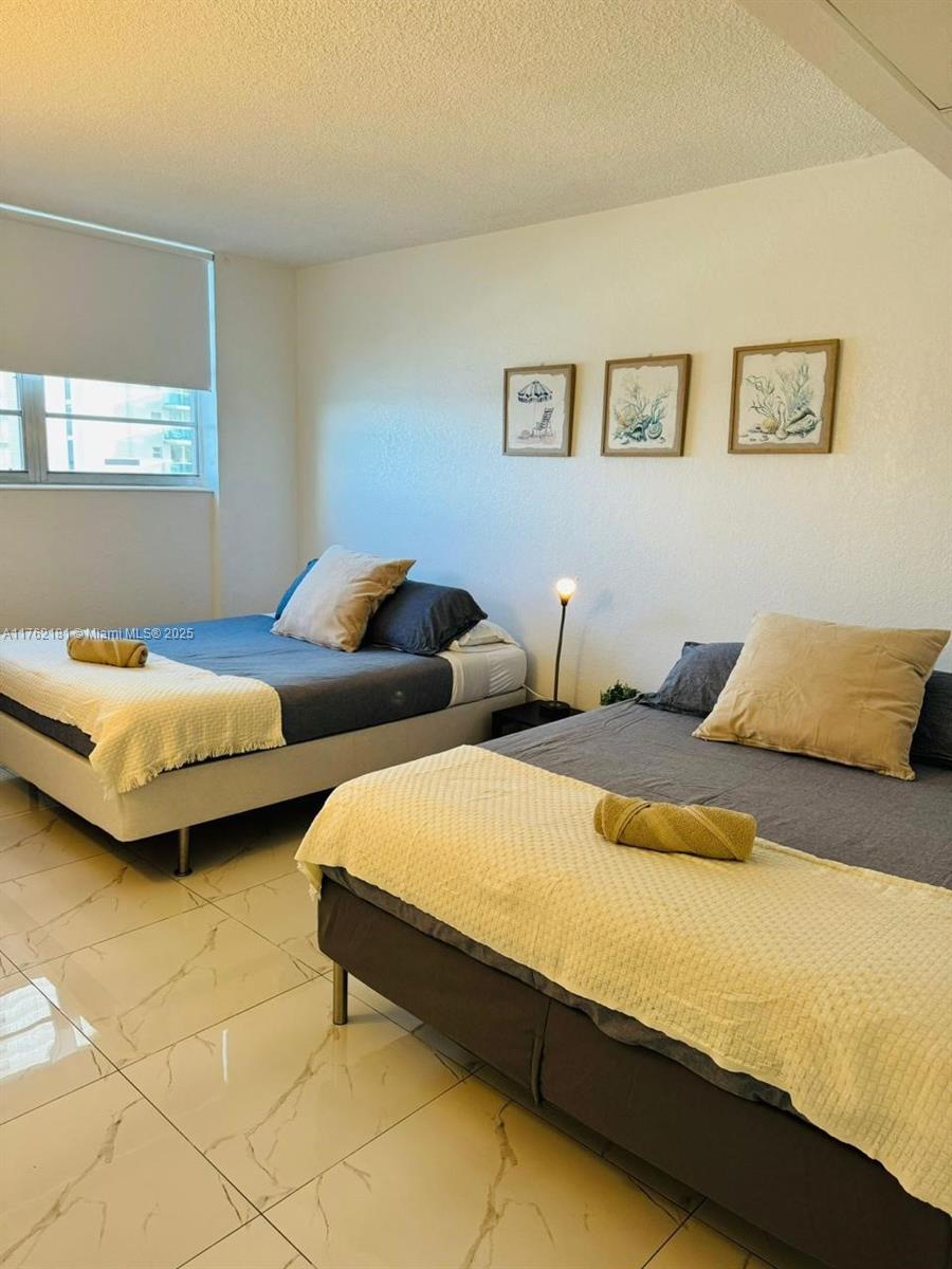 A bedroom features two beds with gray bedding, beige throws, and light-colored tile flooring — 3901 S Ocean Dr # 10G, Hollywood FL 33019, HOLLYWOOD, FL