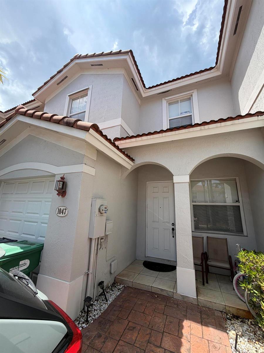 A two-story townhouse exterior features a white garage, arched entryway, and a tiled walkway — 1047 NE 208th Street, Miami FL 33179, MIAMI, FL