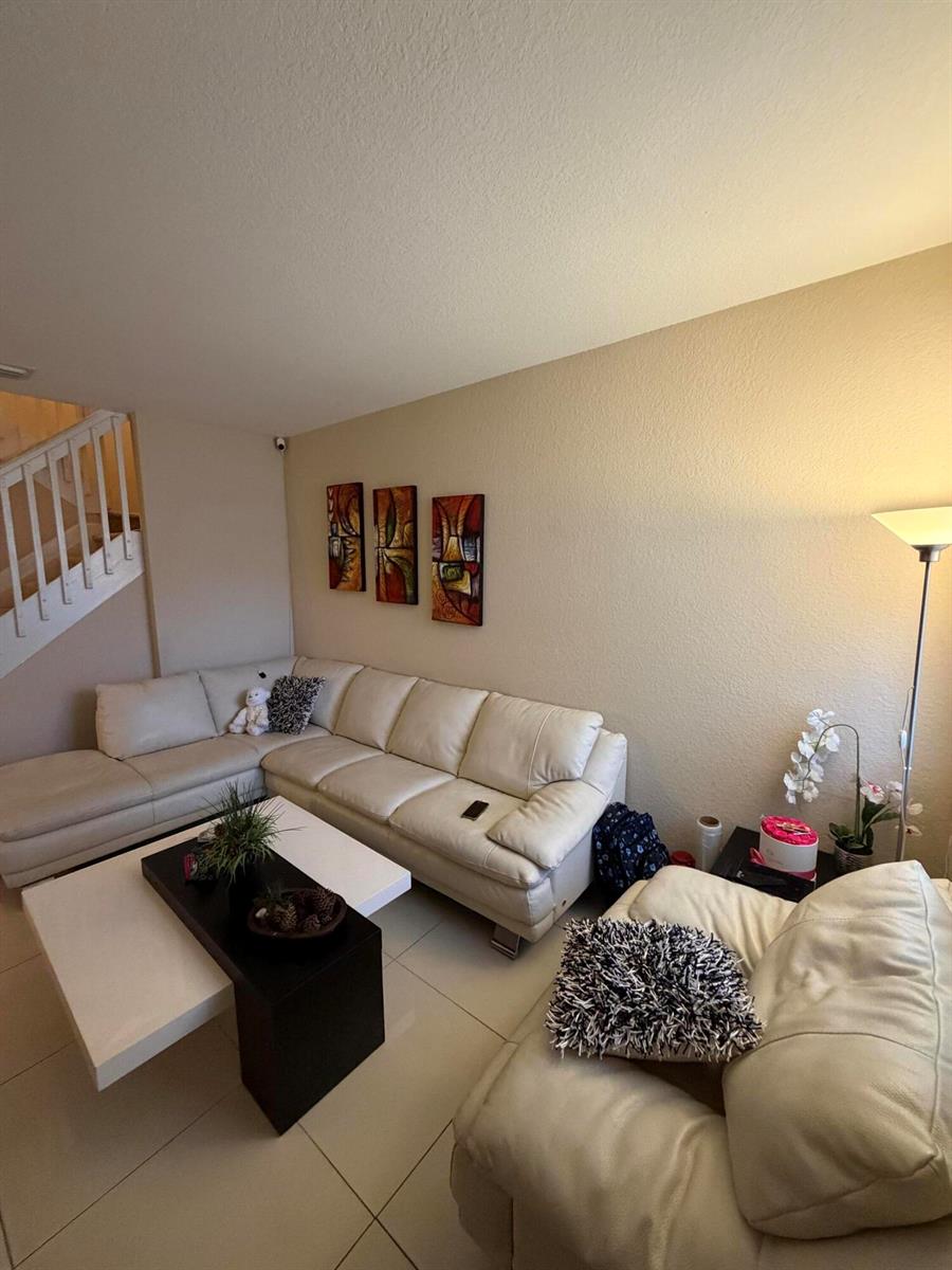 A living room features a white sectional sofa, a nested coffee table, and wall art — 1047 NE 208th Street, Miami FL 33179, MIAMI, FL