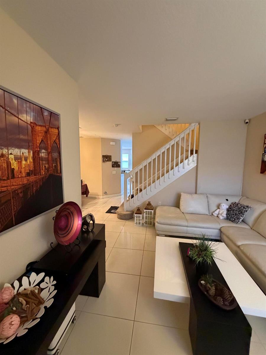 A living room features white tile flooring, a white sectional sofa, and a staircase — 1047 NE 208th Street, Miami FL 33179, MIAMI, FL