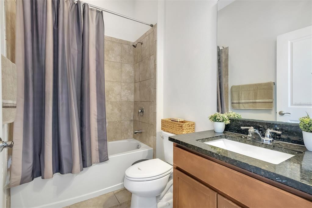 A bathroom features a shower-tub combo with beige tile, a toilet, and a granite vanity — 15807 SWEET LEMON WAY, WINTER GARDEN, FL