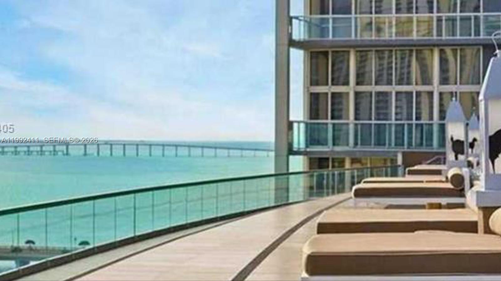 A balcony with lounge chairs overlooks the ocean and a bridge — 465 Brickell Ave # 5605, Miami FL 33131, MIAMI, FL