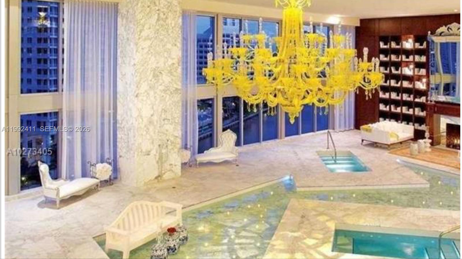 A large, high-ceilinged room features an indoor pool, a yellow chandelier, and floor-to-ceiling windows — 465 Brickell Ave # 5605, Miami FL 33131, MIAMI, FL