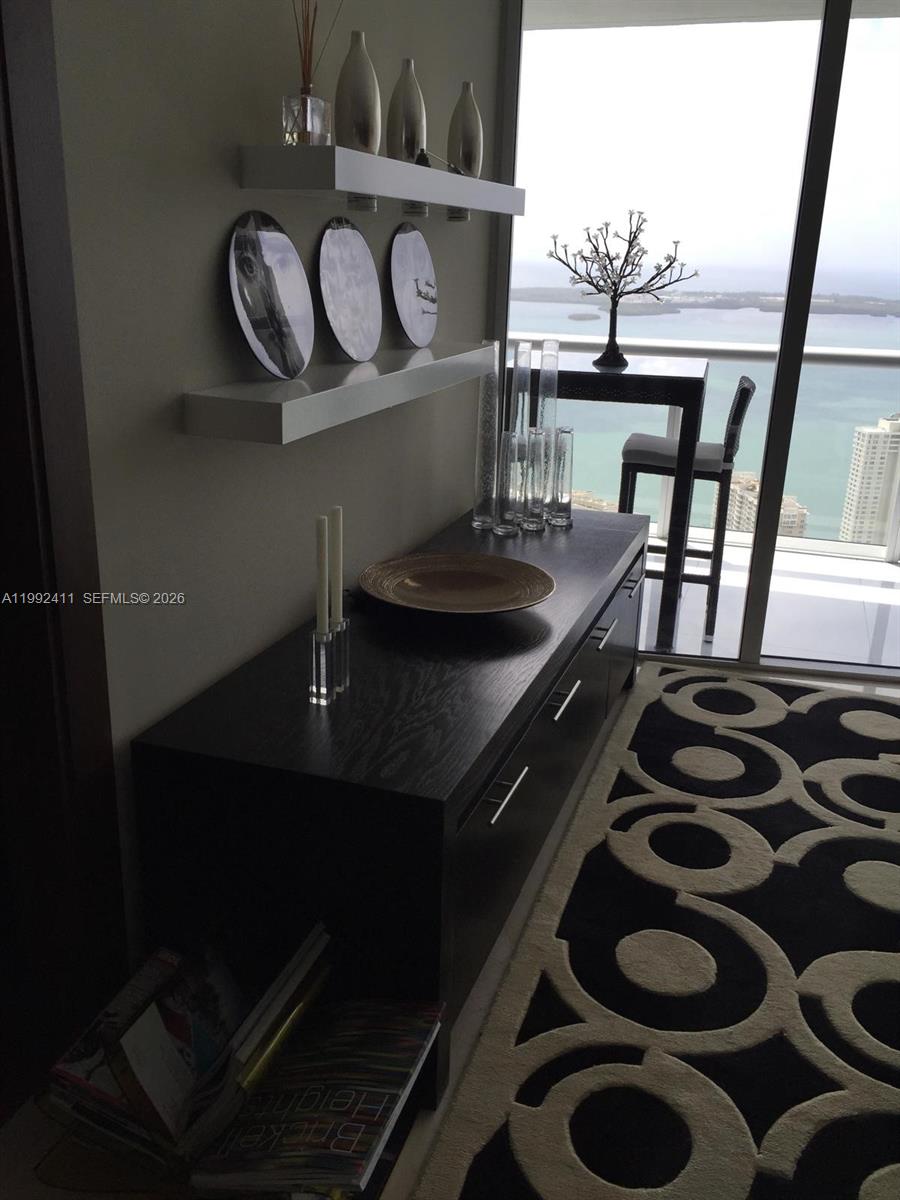 A modern room features a dark wood console, floating shelves with decor, and a balcony view — 465 Brickell Ave # 5605, Miami FL 33131, MIAMI, FL