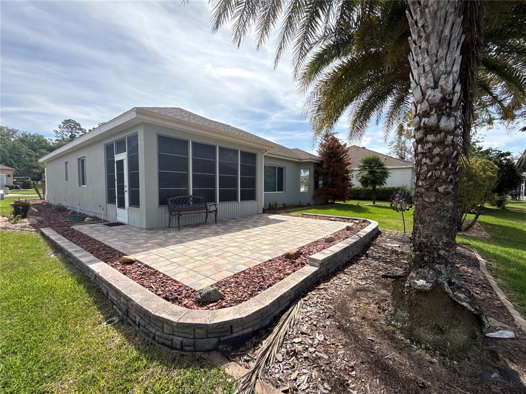 A paved patio with a retaining wall sits beside a house with a screened-in porch — 9484 SE 124TH LOOP, SUMMERFIELD, FL