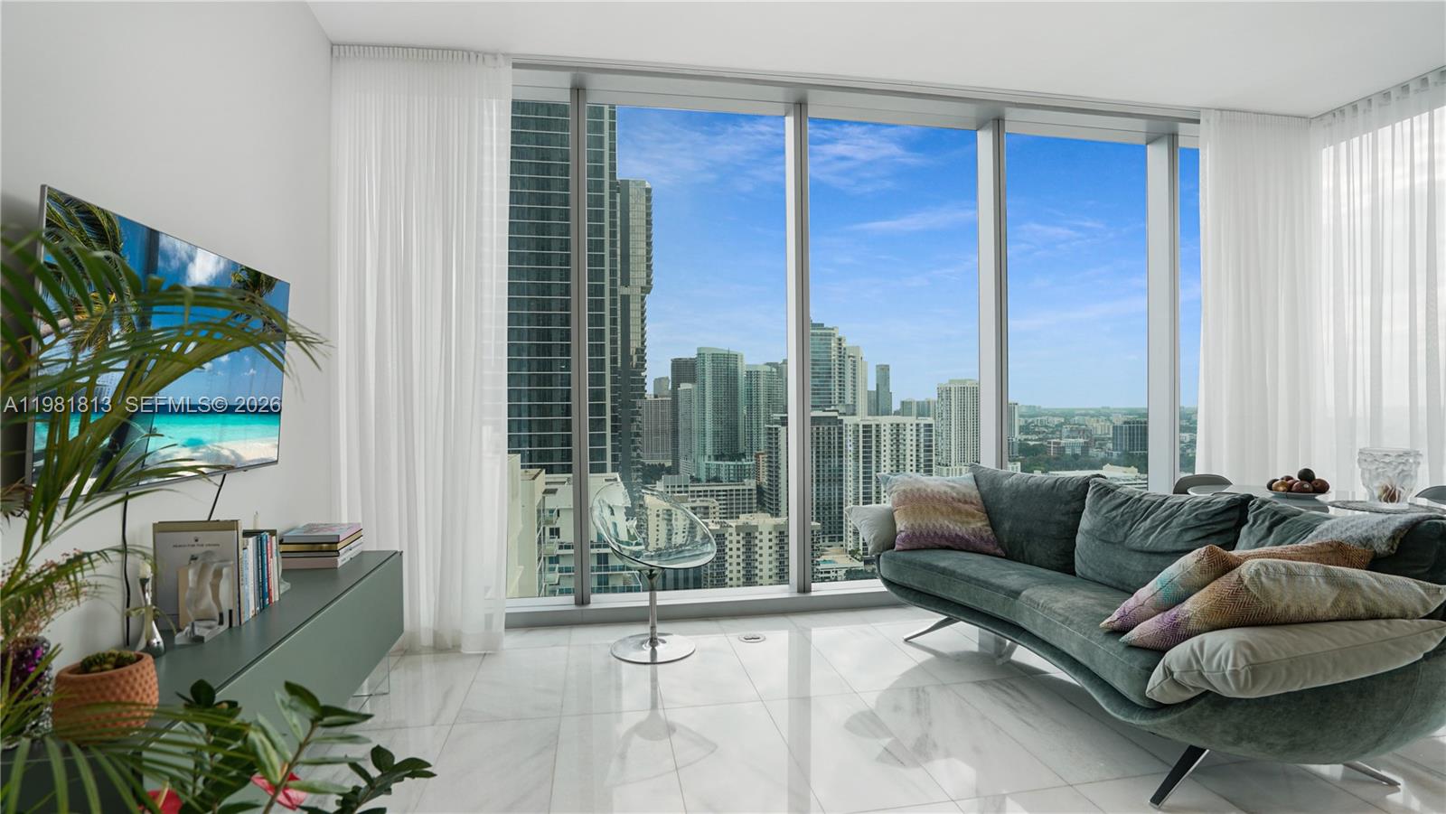 A modern living room features a curved sofa, floor-to-ceiling windows, and a city skyline view — 700 NE 26th Ter # 3005, Miami FL 33137, MIAMI, FL