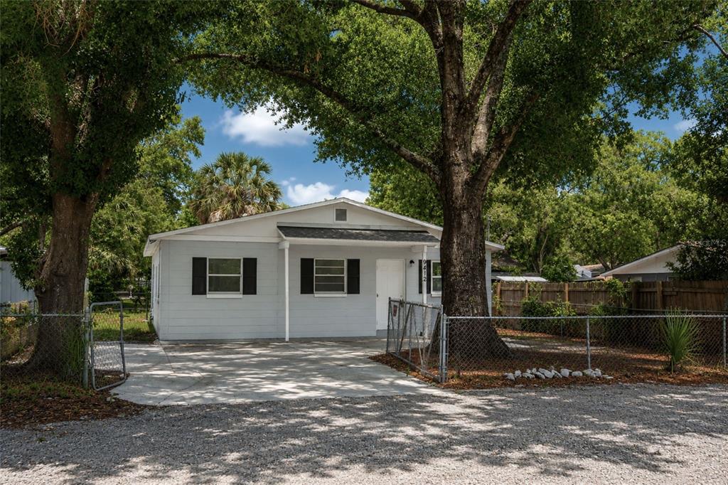 A light blue single-story house with black shutters sits behind a chain-link fence and trees — 9412 N ELMER STREET, TAMPA, FL