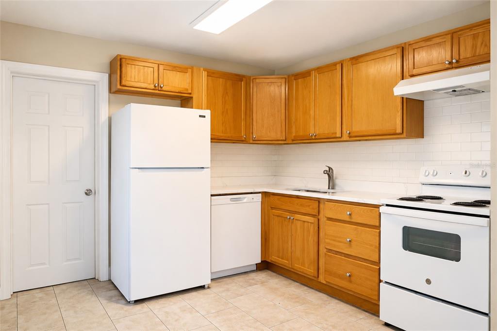 A kitchen features light wood cabinets, white appliances, white subway tile backsplash, and tile flooring — 9412 N ELMER STREET, TAMPA, FL
