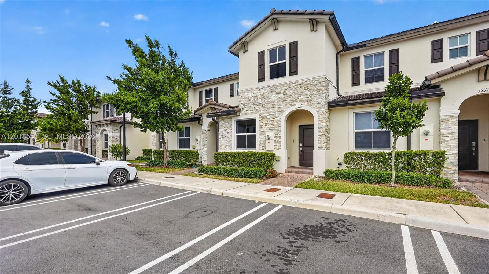 A two-story townhouse with a stone facade, brown shutters, and a paved parking area — 12123 NW 23rd Ct, Miami FL 33167, MIAMI, FL