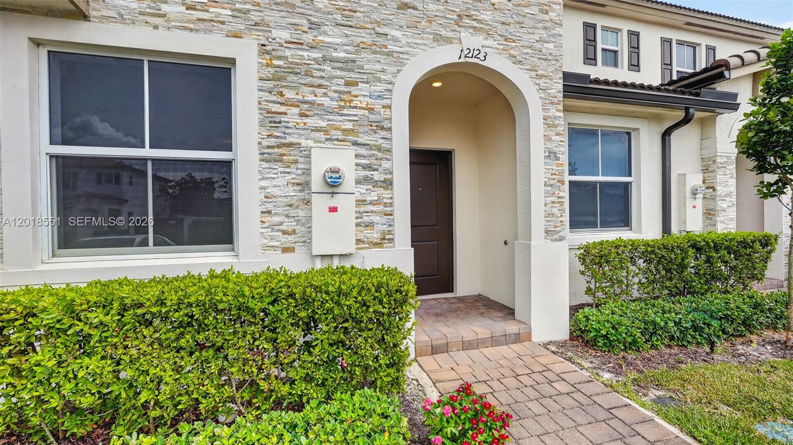 The exterior of a townhouse features a stone facade, an arched entryway, and landscaped bushes — 12123 NW 23rd Ct, Miami FL 33167, MIAMI, FL