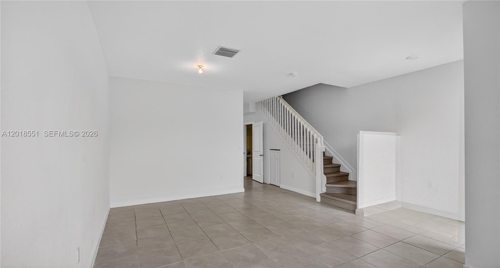 An empty room features light-colored tile flooring, white walls, and a staircase with white railings — 12123 NW 23rd Ct, Miami FL 33167, MIAMI, FL