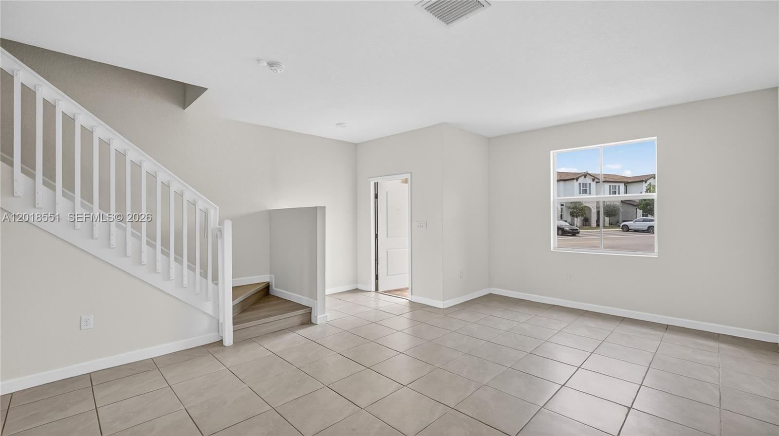 An empty room features light-colored tile flooring, a white staircase, and a single window — 12123 NW 23rd Ct, Miami FL 33167, MIAMI, FL