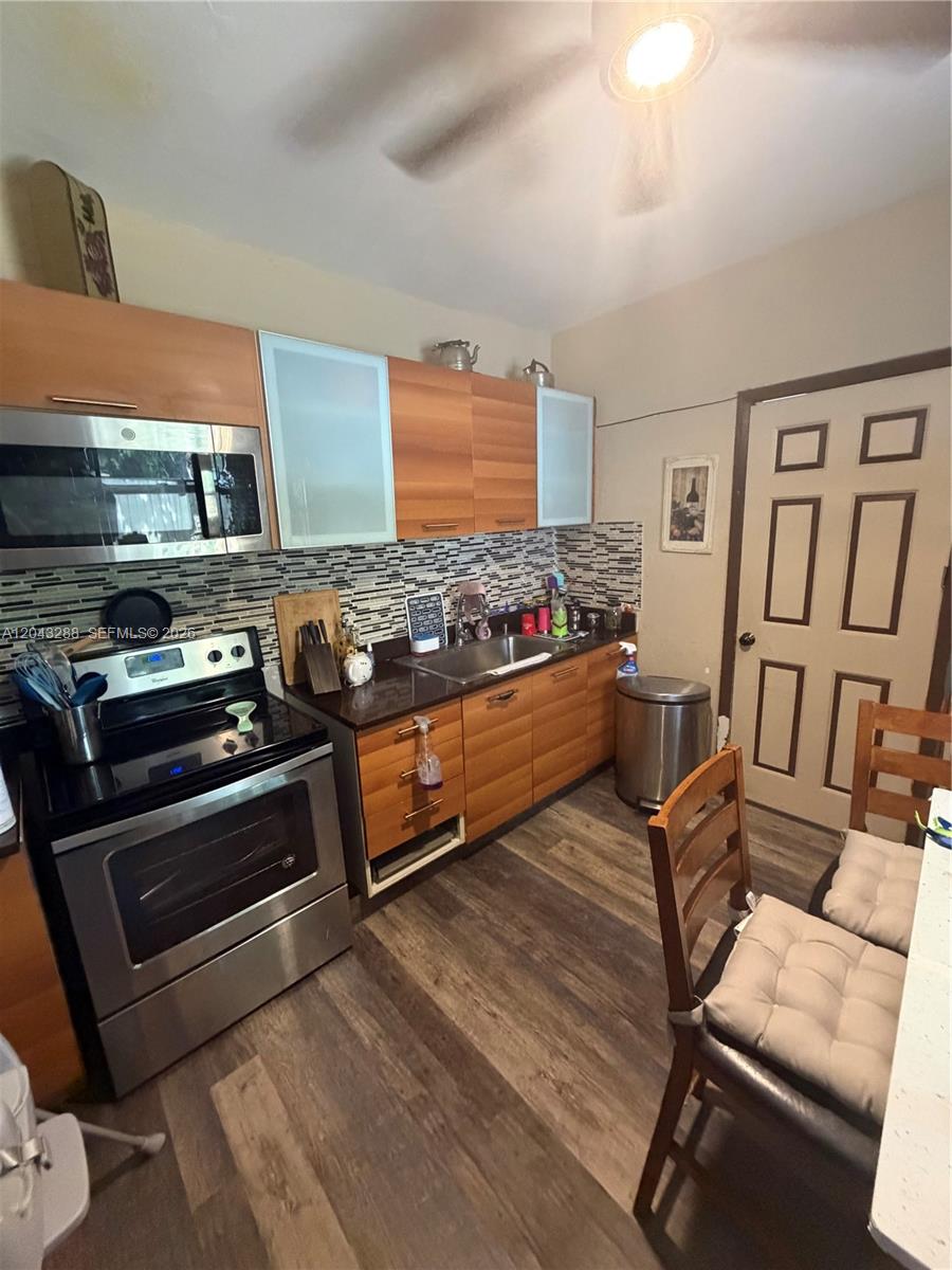 A kitchen features wood-toned cabinets, stainless steel appliances, a mosaic backsplash, and wood-look flooring — MIAMI, FL