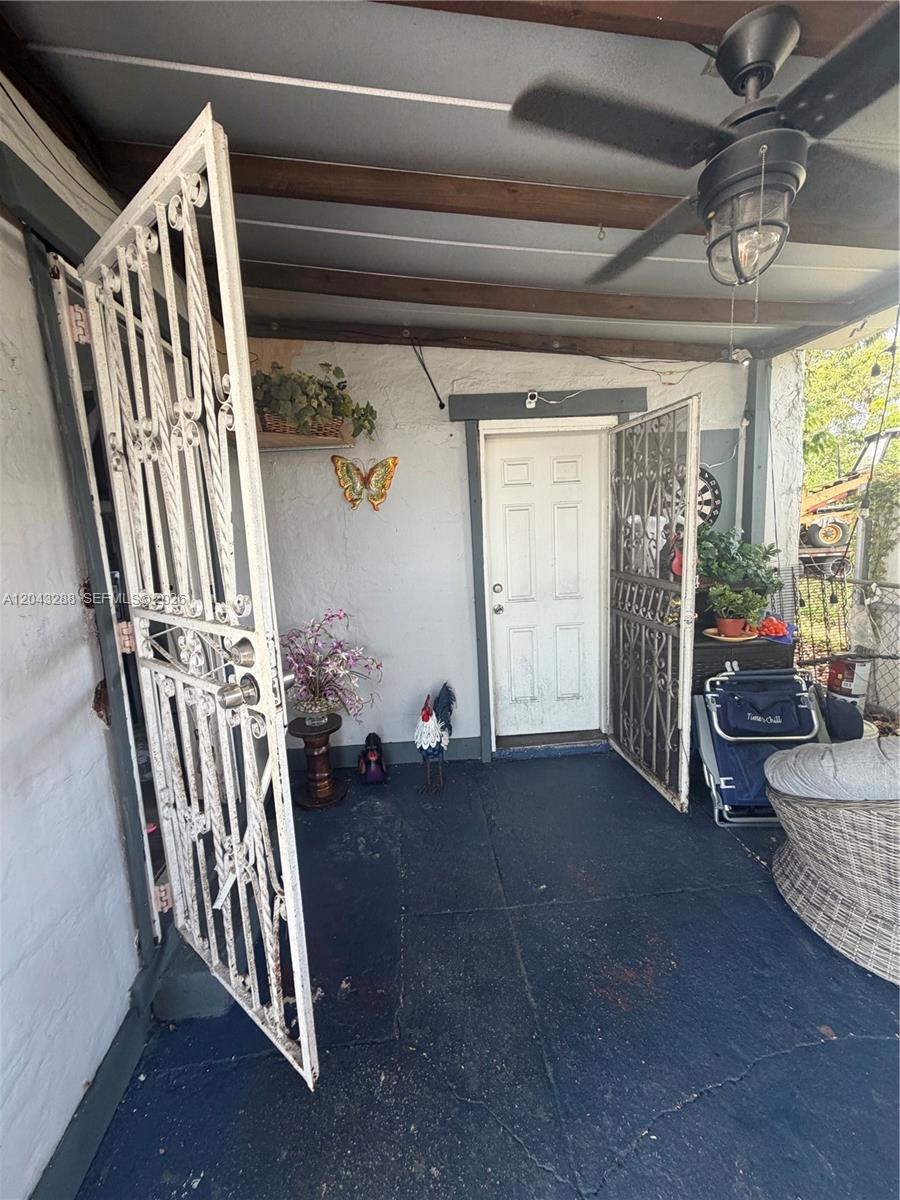 A covered porch features a white door, decorative metal security gates, and a ceiling fan — MIAMI, FL