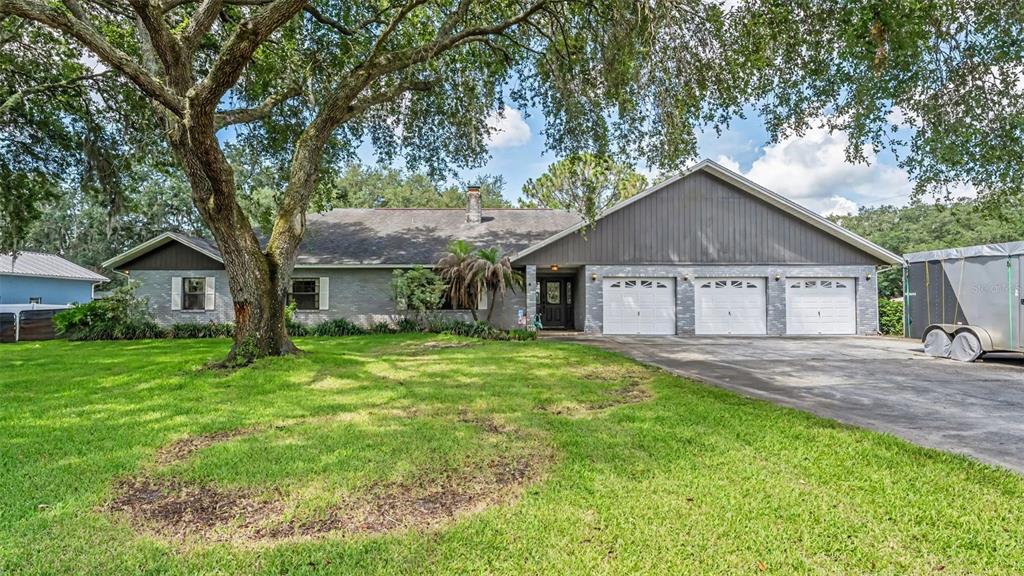 A single-story house with a gray brick exterior, three garage doors, and a large front tree — 14080 US HIGHWAY 98 N, KATHLEEN, FL