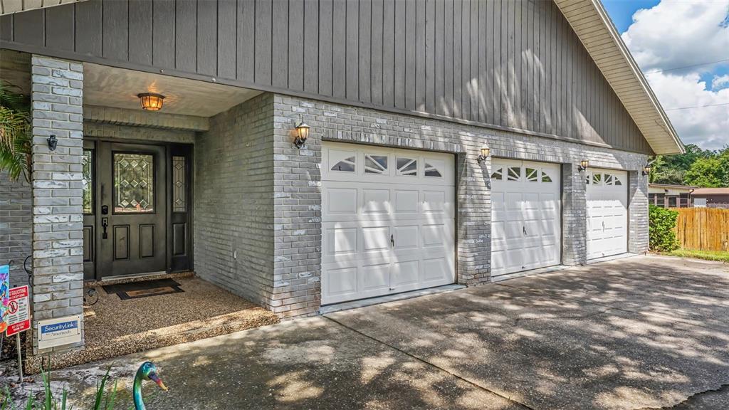 A house exterior features a gray brick facade, a dark front door, and three garage doors — 14080 US HIGHWAY 98 N, KATHLEEN, FL
