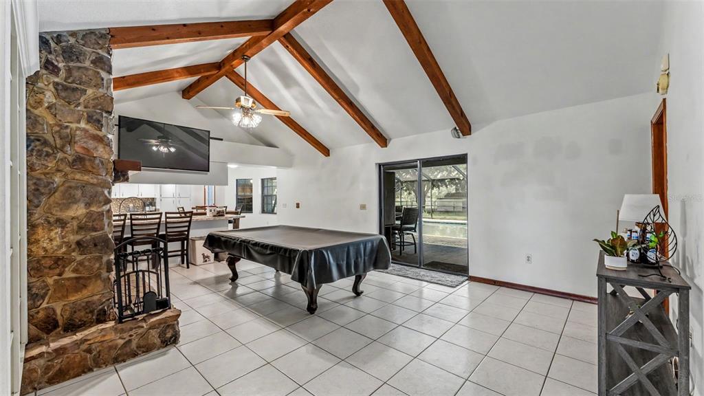 A living room features a stone fireplace, vaulted wood-beamed ceilings, tile floors, and a pool table — 14080 US HIGHWAY 98 N, KATHLEEN, FL