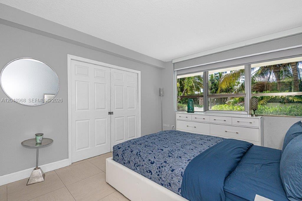 A bedroom features a bed with blue bedding, a white dresser, and a round mirror — 1500 Bay Rd # 128S, Miami Beach FL 33139, MIAMI BEACH, FL