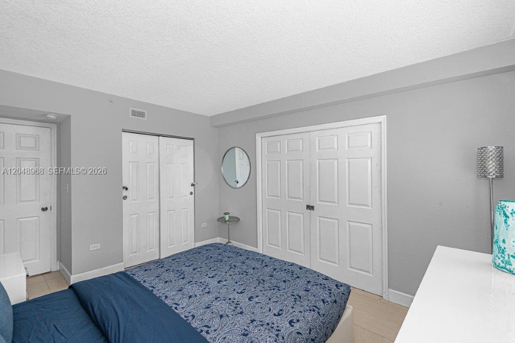 A bedroom features gray walls, white closet doors, and a bed with a blue patterned comforter — 1500 Bay Rd # 128S, Miami Beach FL 33139, MIAMI BEACH, FL