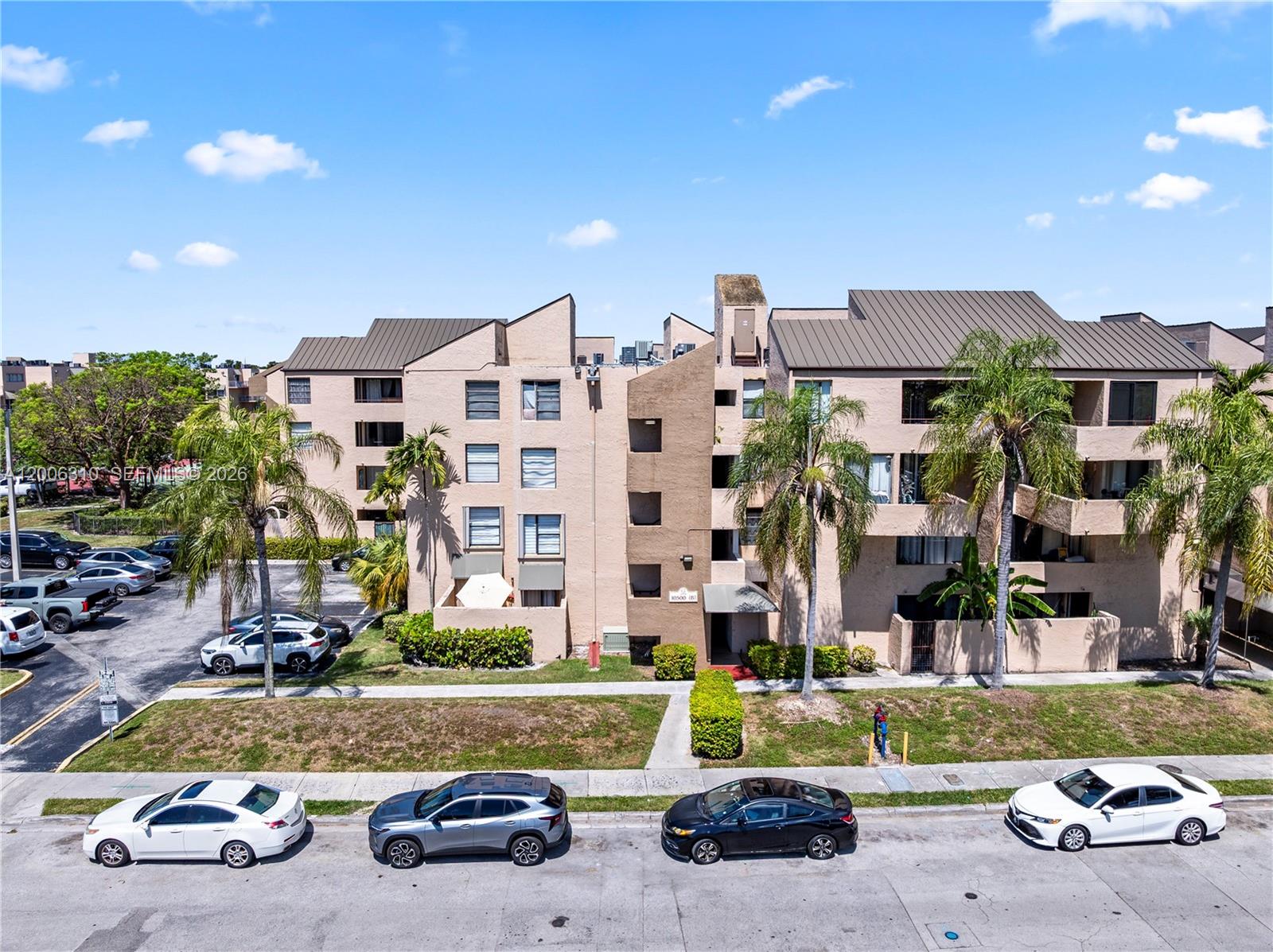 An exterior view of a multi-story apartment building with palm trees and parked cars — 10500 SW 108th Ave # B211, Miami FL 33176, MIAMI, FL