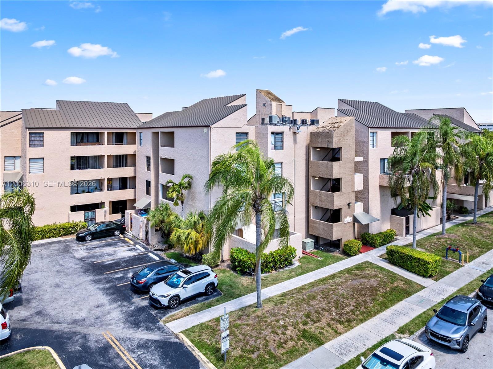 An exterior view of a multi-story apartment complex with a parking lot and palm trees — 10500 SW 108th Ave # B211, Miami FL 33176, MIAMI, FL