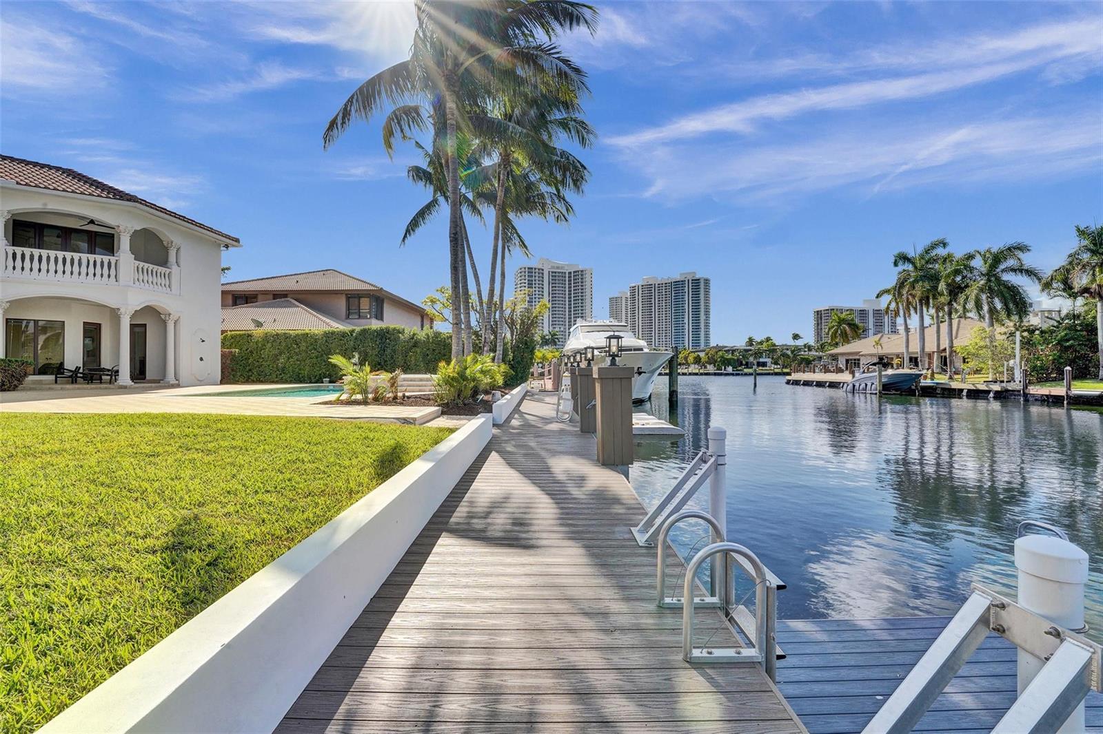 A wooden dock extends along a canal beside a white house with a pool — 642 Palm Drive, Hallandale Beach FL 33009, HALLANDALE BEACH, FL