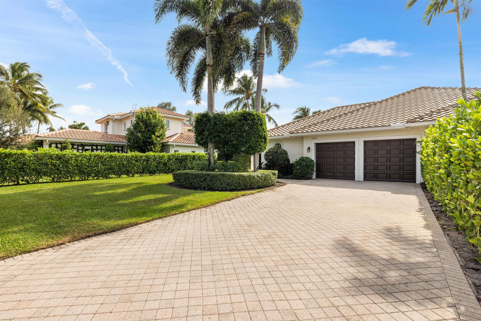 A paved driveway leads to a two-car garage in front of a house with palm trees — 14270 Calypso Lane, Wellington FL 33414, WELLINGTON, FL