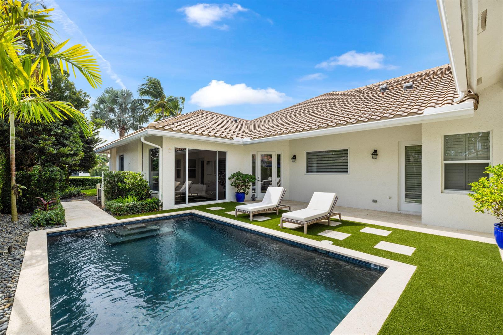 A backyard features a swimming pool, two lounge chairs, and artificial turf beside a house — 14270 Calypso Lane, Wellington FL 33414, WELLINGTON, FL