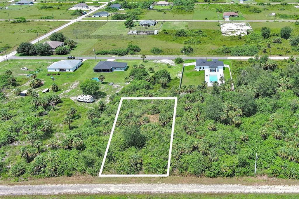 An aerial view shows a rectangular vacant lot outlined in white amidst surrounding vegetation — 1507 HINES AVENUE, LEHIGH ACRES, FL