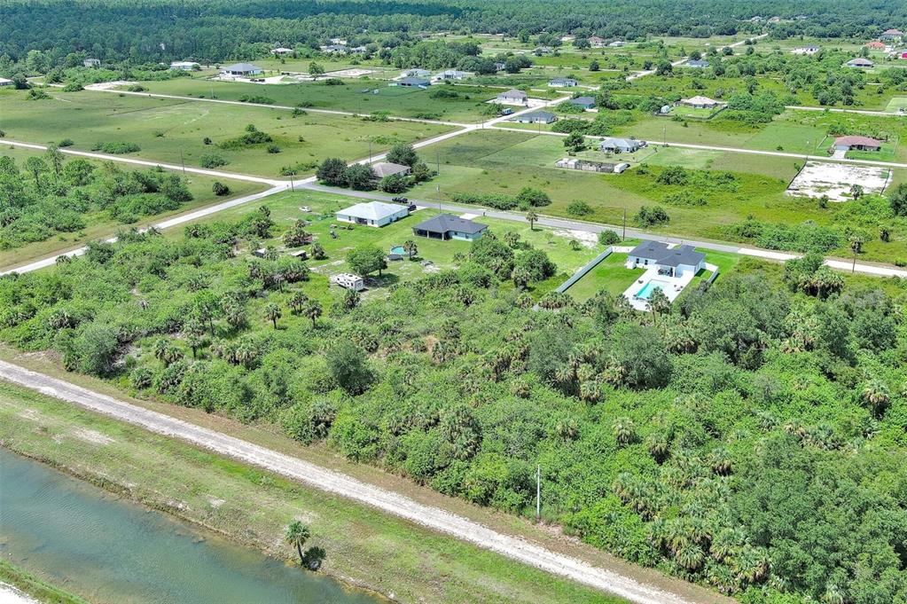 An aerial view shows several houses surrounded by dense vegetation and a canal — 1507 HINES AVENUE, LEHIGH ACRES, FL