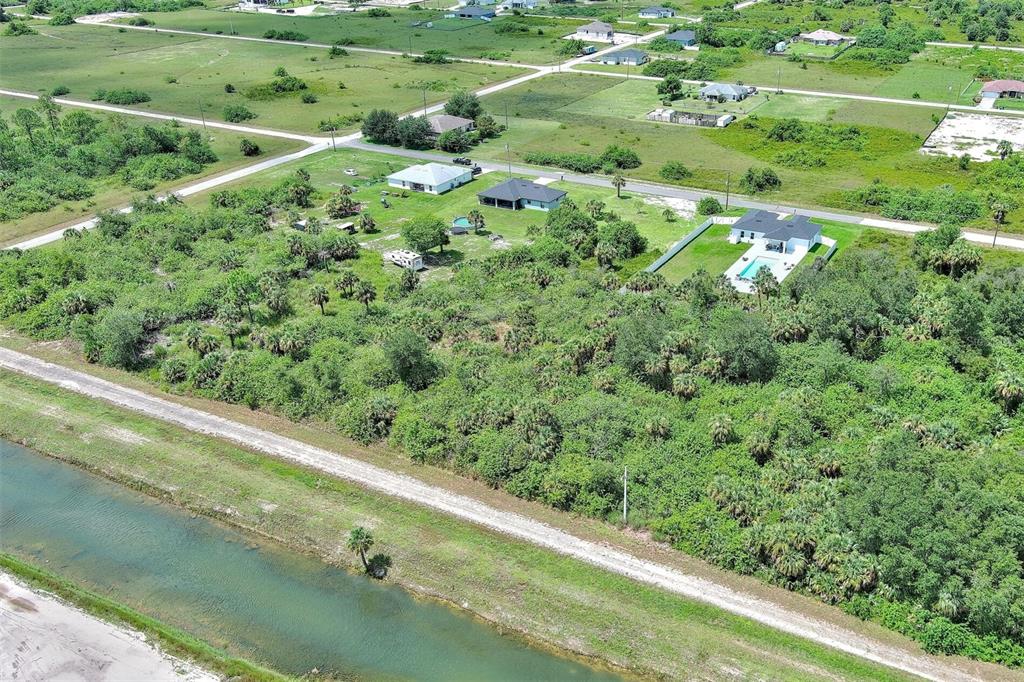 An aerial view shows a residential lot with dense vegetation, a canal, and nearby houses — 1507 HINES AVENUE, LEHIGH ACRES, FL