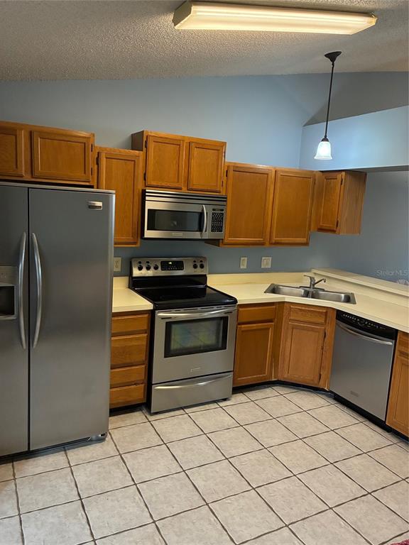 A kitchen features oak cabinets, stainless steel appliances, light countertops, and tiled flooring — 5433 LAKE MARGARET DRIVE UNIT E 195, ORLANDO, FL