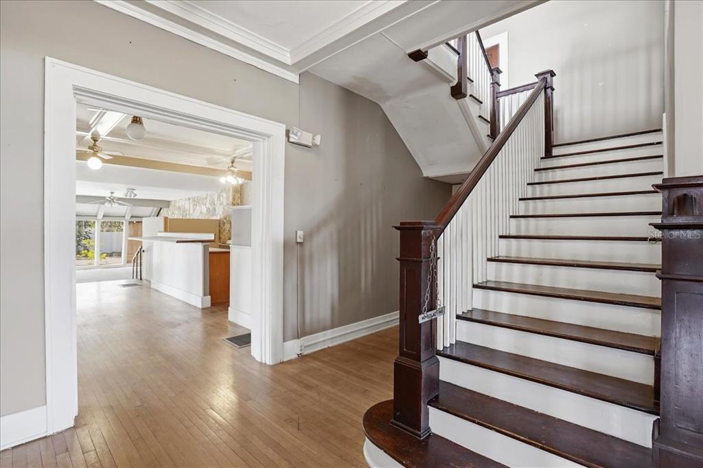 A wooden staircase with white spindles stands beside an entryway leading to a kitchen area — 337 8TH AVENUE W, PALMETTO, FL