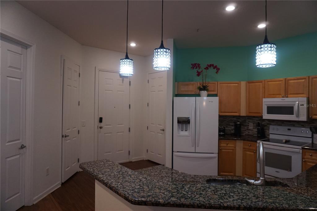 A kitchen features granite countertops, light wood cabinets, white appliances, and three hanging pendant lights — 719 TERRACE RIDGE CIRCLE UNIT 719, DAVENPORT, FL