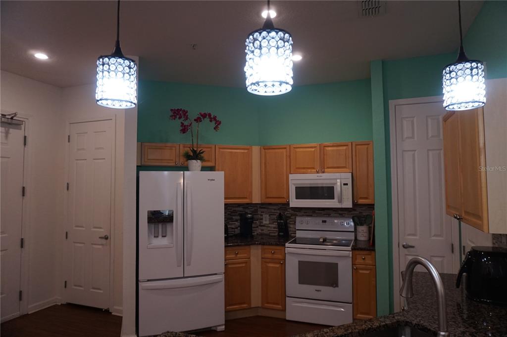 A kitchen features light wood cabinets, white appliances, granite countertops, and three crystal pendant lights — 719 TERRACE RIDGE CIRCLE UNIT 719, DAVENPORT, FL