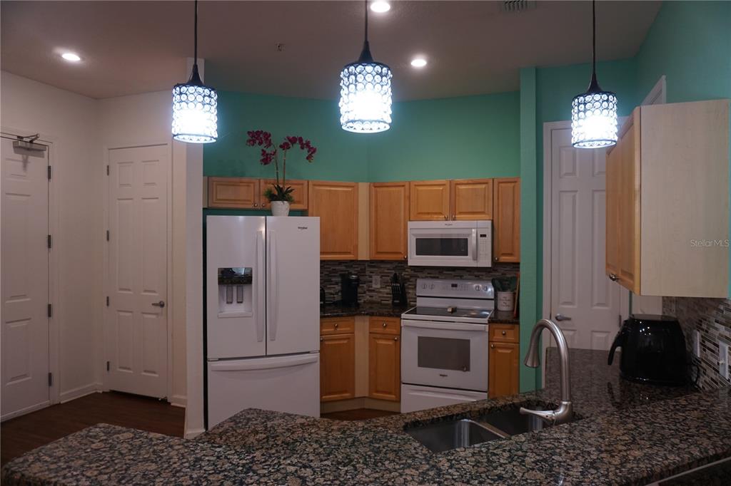 A kitchen features light wood cabinets, granite countertops, white appliances, and three pendant lights — 719 TERRACE RIDGE CIRCLE UNIT 719, DAVENPORT, FL