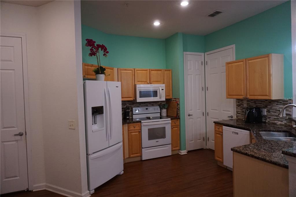 A kitchen features light wood cabinets, white appliances, granite countertops, and teal-painted walls — 719 TERRACE RIDGE CIRCLE UNIT 719, DAVENPORT, FL
