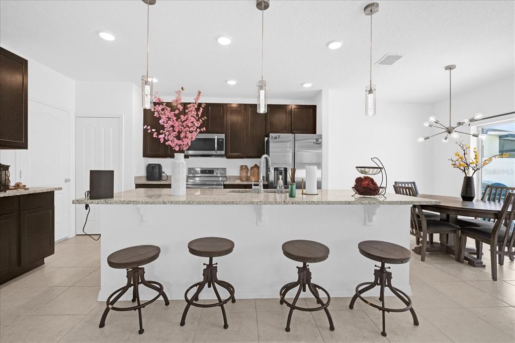 A kitchen features dark wood cabinets, a granite island with four stools, and pendant lighting — 4432 DESERT ROSE AVENUE, KISSIMMEE, FL